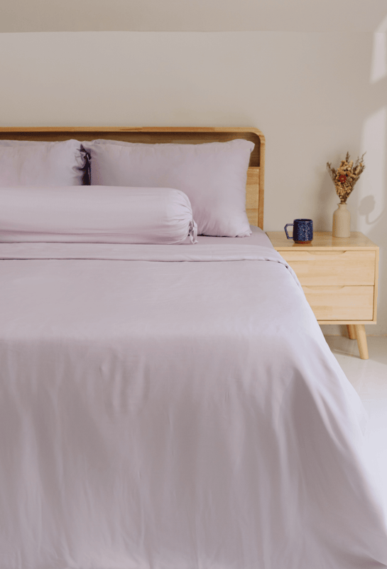 Bed with light purple bedding and wooden headboard and nightstand.