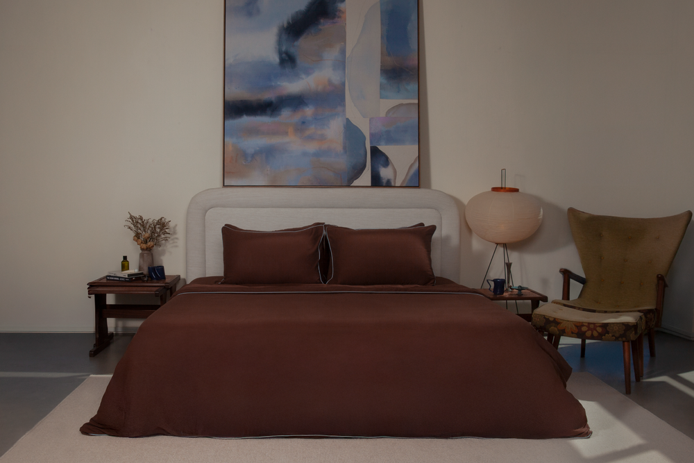 Bedroom with brown bedding, white headboard, and abstract painting on wall.